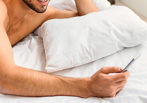 Mann mit Handy auf dem Bett
